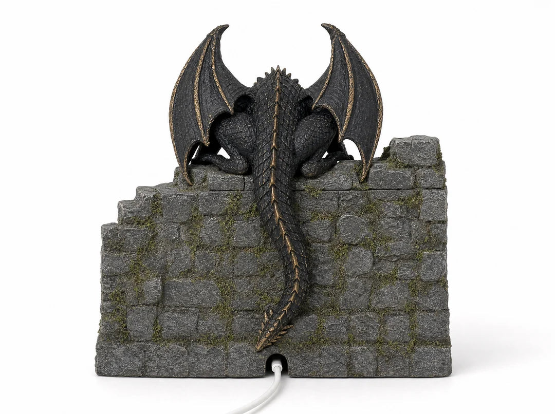Rear view showing the dragon's sculpted scales, raised wings and long tail against the stone castle wall